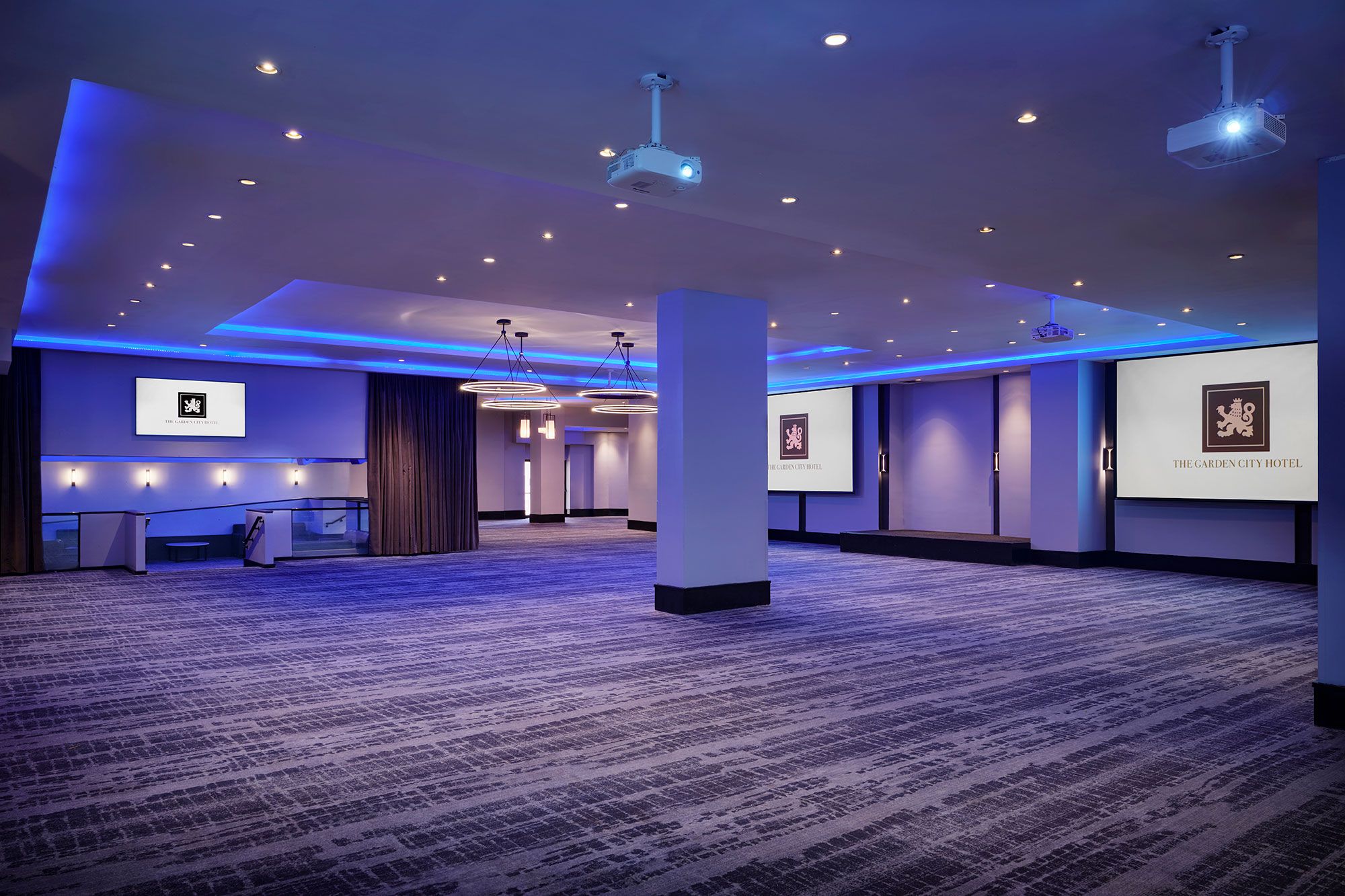 Un amplio vestíbulo de hotel con piso alfombrado, iluminación empotrada y una gran pantalla que muestra el nombre del hotel.