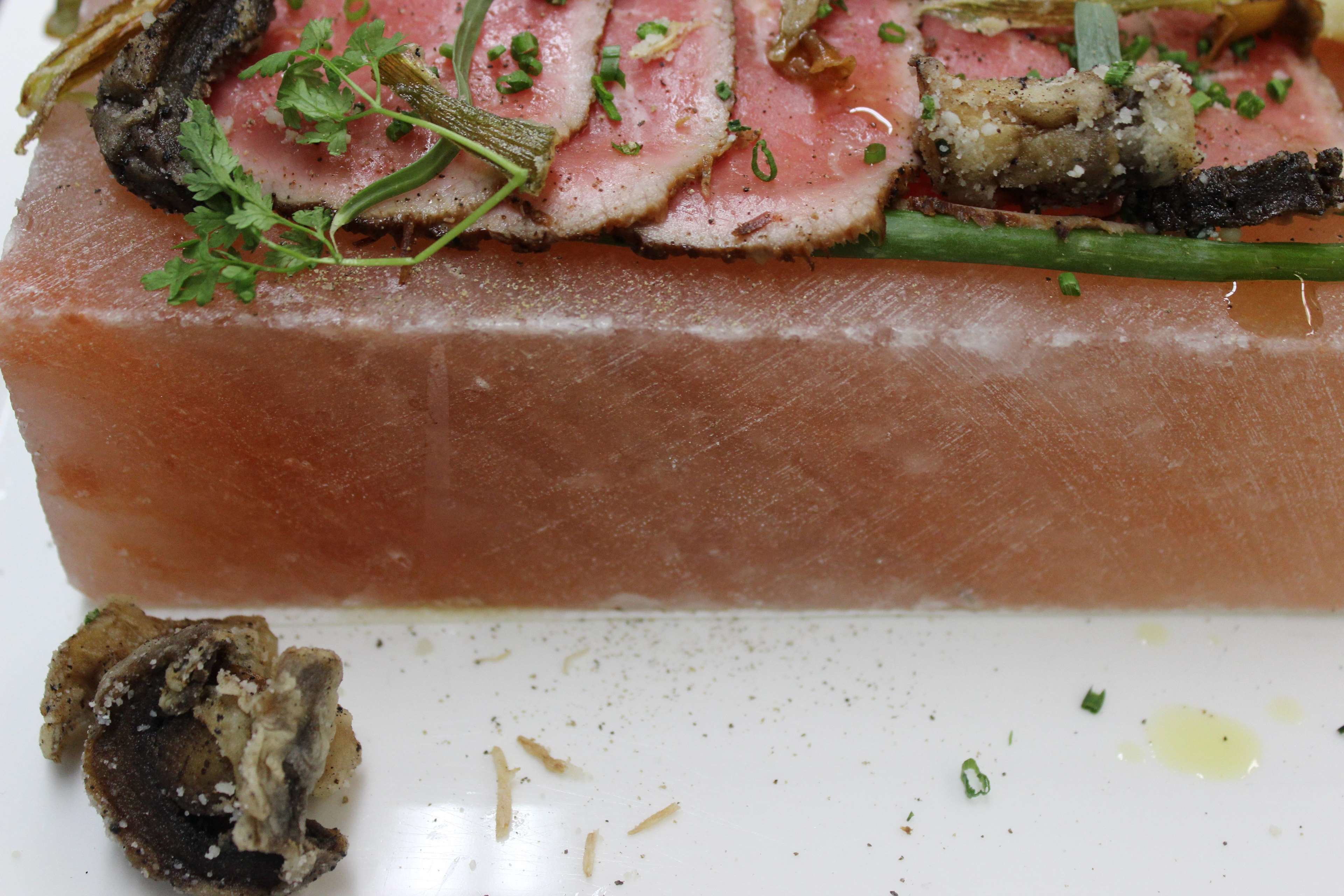 A dish with sliced meat, herbs, and mushrooms on a white plate.