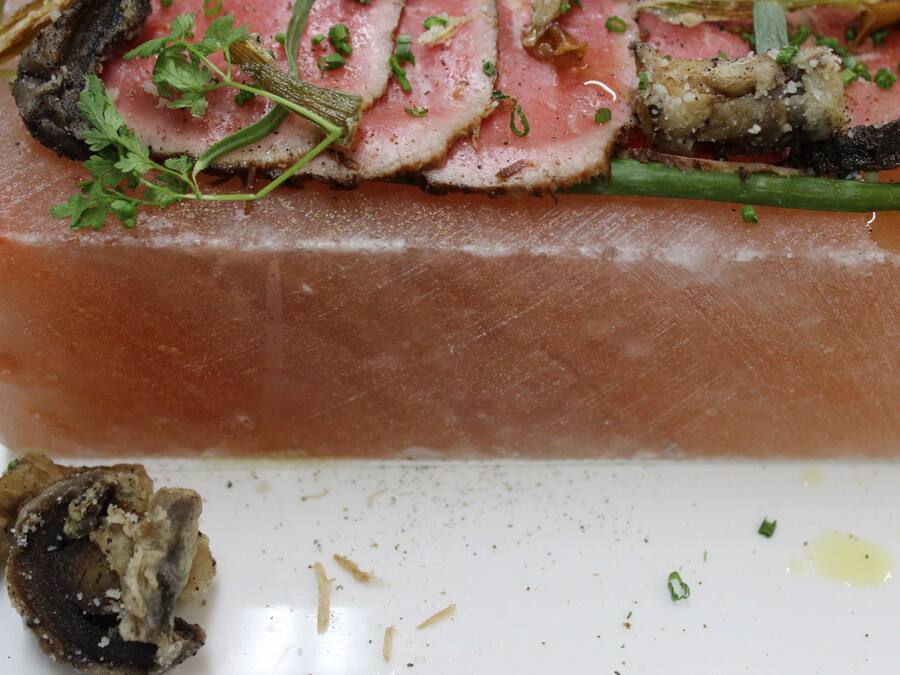 A dish with sliced meat, herbs, and mushrooms on a white plate.