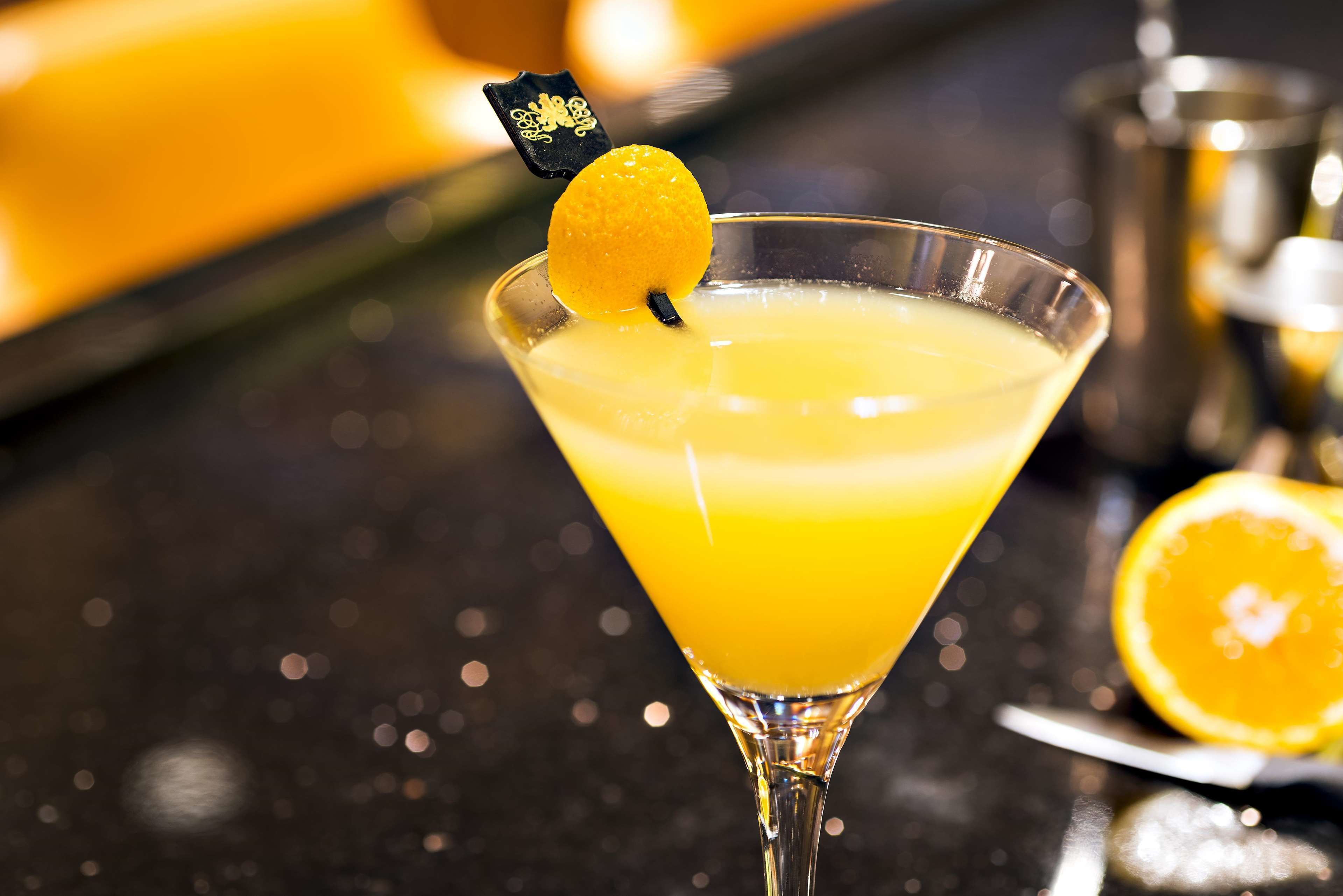 Una copa de martini con un adorno de limón sobre una barra.