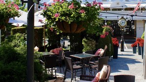 An outdoor seating area with wicker furniture, a hanging flower planter, and a clock.