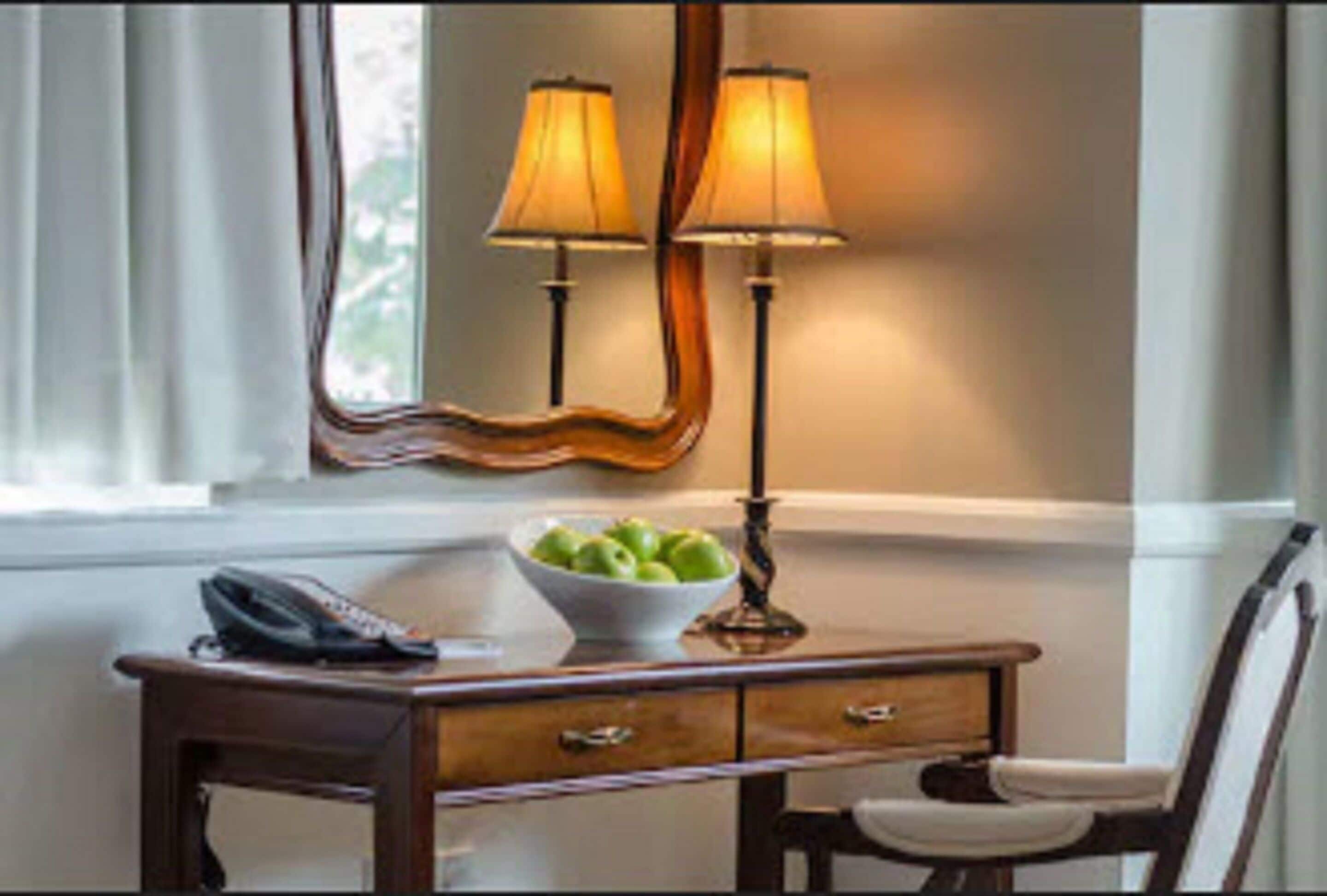 Een houten bureau met een schaal groene appels, een telefoon en twee lampen.