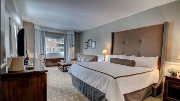 A hotel room with a large bed, a desk, a chair, and a window with curtains.