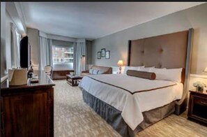 A hotel room with a large bed, a desk, a chair, and a window with curtains. - The Garden City Hotel (Garden City)