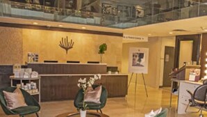 A lobby with a reception desk, green chairs, a coffee table with a plant, and a glass railing in the background.