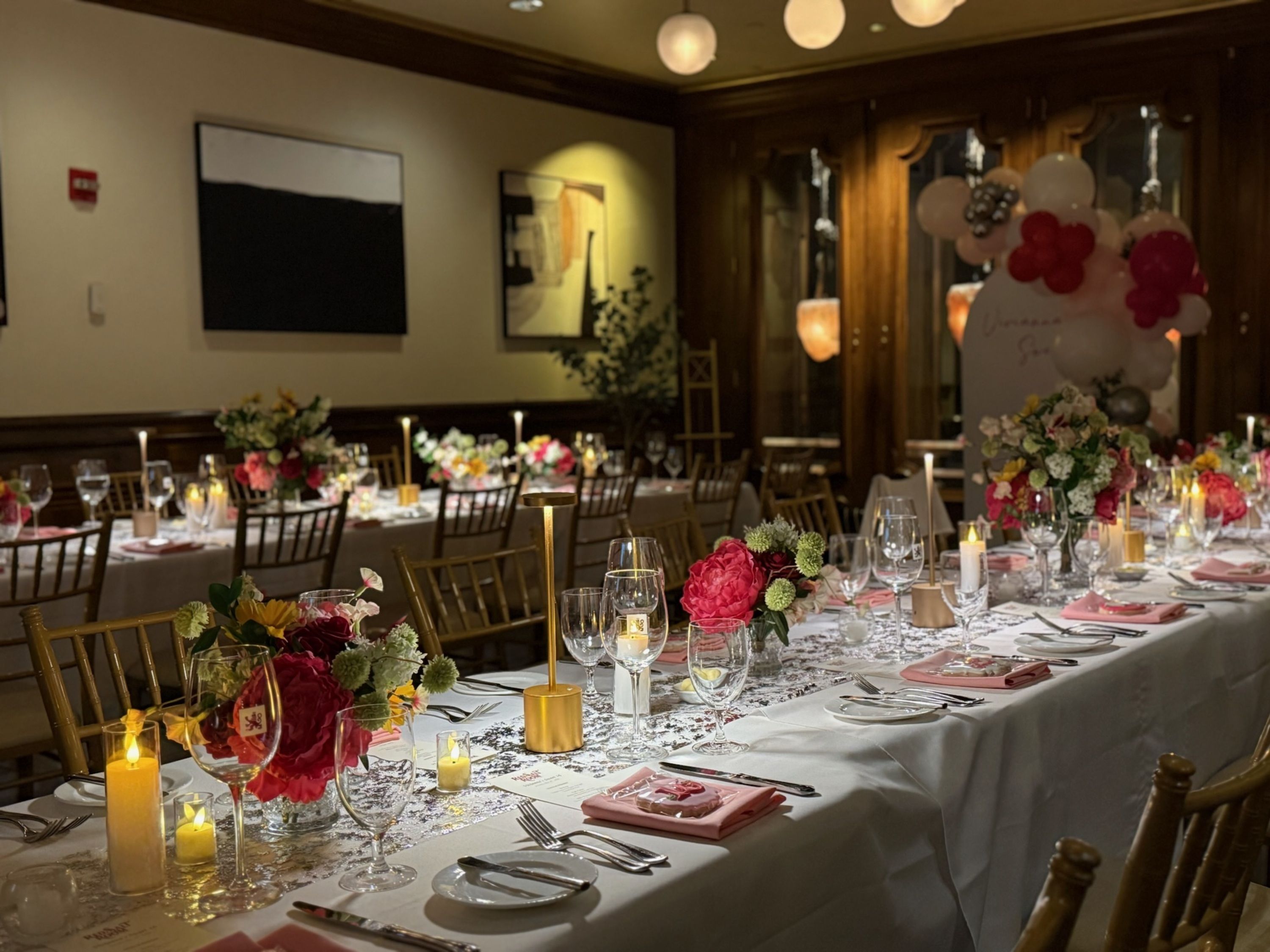 A banquet hall with tables set for a formal event, featuring floral centerpieces, candles, and elegant tableware.