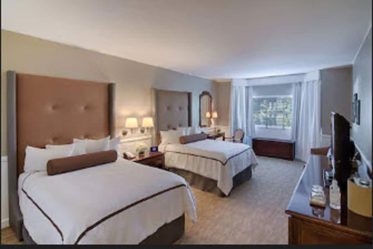 Une chambre d’hôtel avec deux lits, un bureau, une télévision et une fenêtre avec des rideaux.