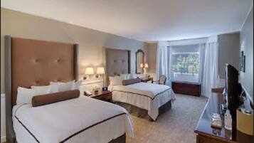 A hotel room with two beds, a desk, a TV, and a window with curtains.