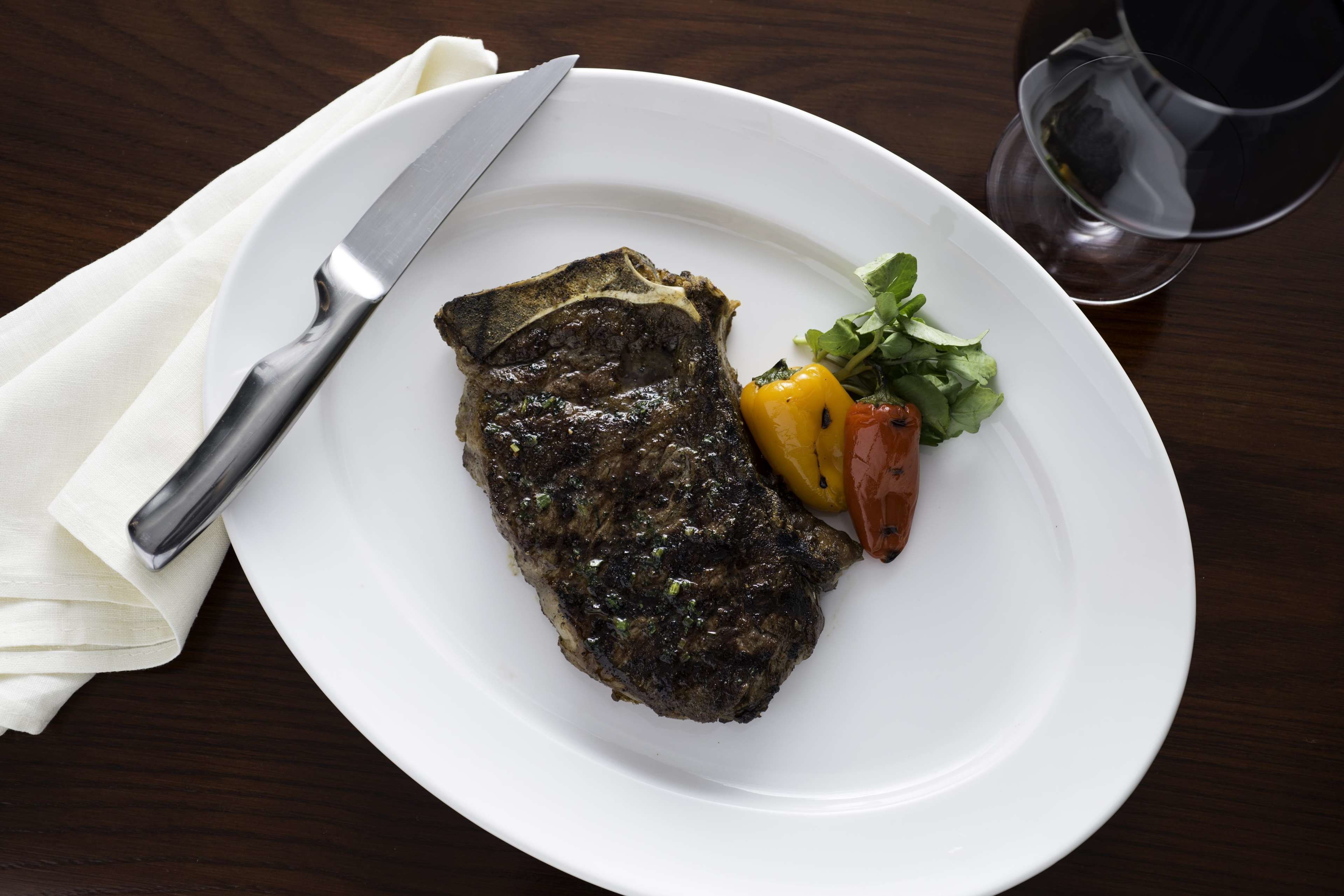 Un plato con un bistec, un cuchillo y algunas verduras sobre una mesa de madera.