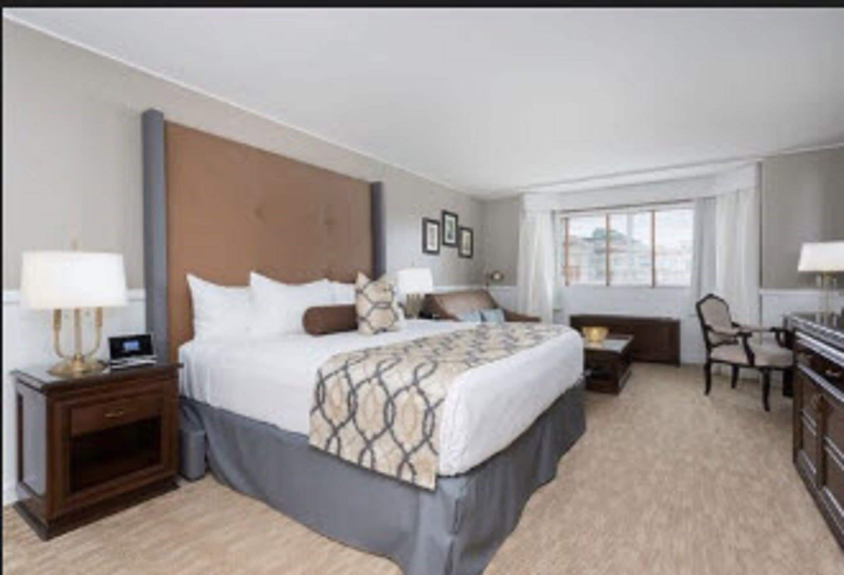 A hotel room with a large bed, a desk, a chair, and a window.