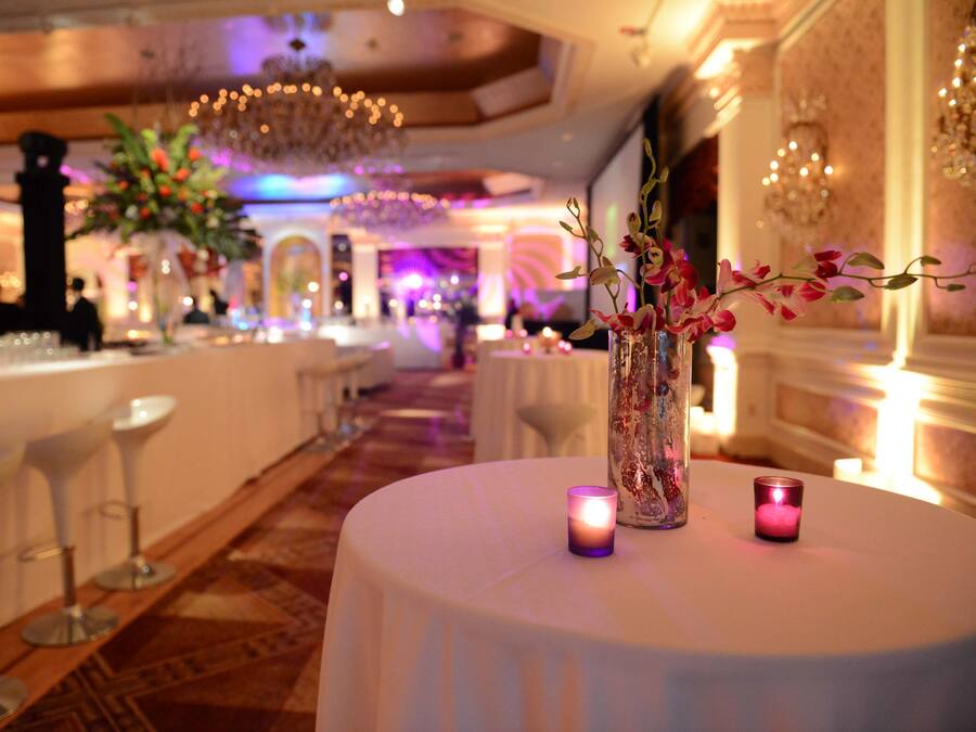 Eine Bar mit weißen Barhocker, einem runden Tisch mit Kerzen und einer Vase mit Blumen.