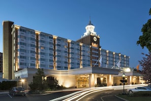 A multi-story hotel with a prominent clock tower, a well-lit entrance, and a landscaped driveway. - The Garden City Hotel (Garden City)