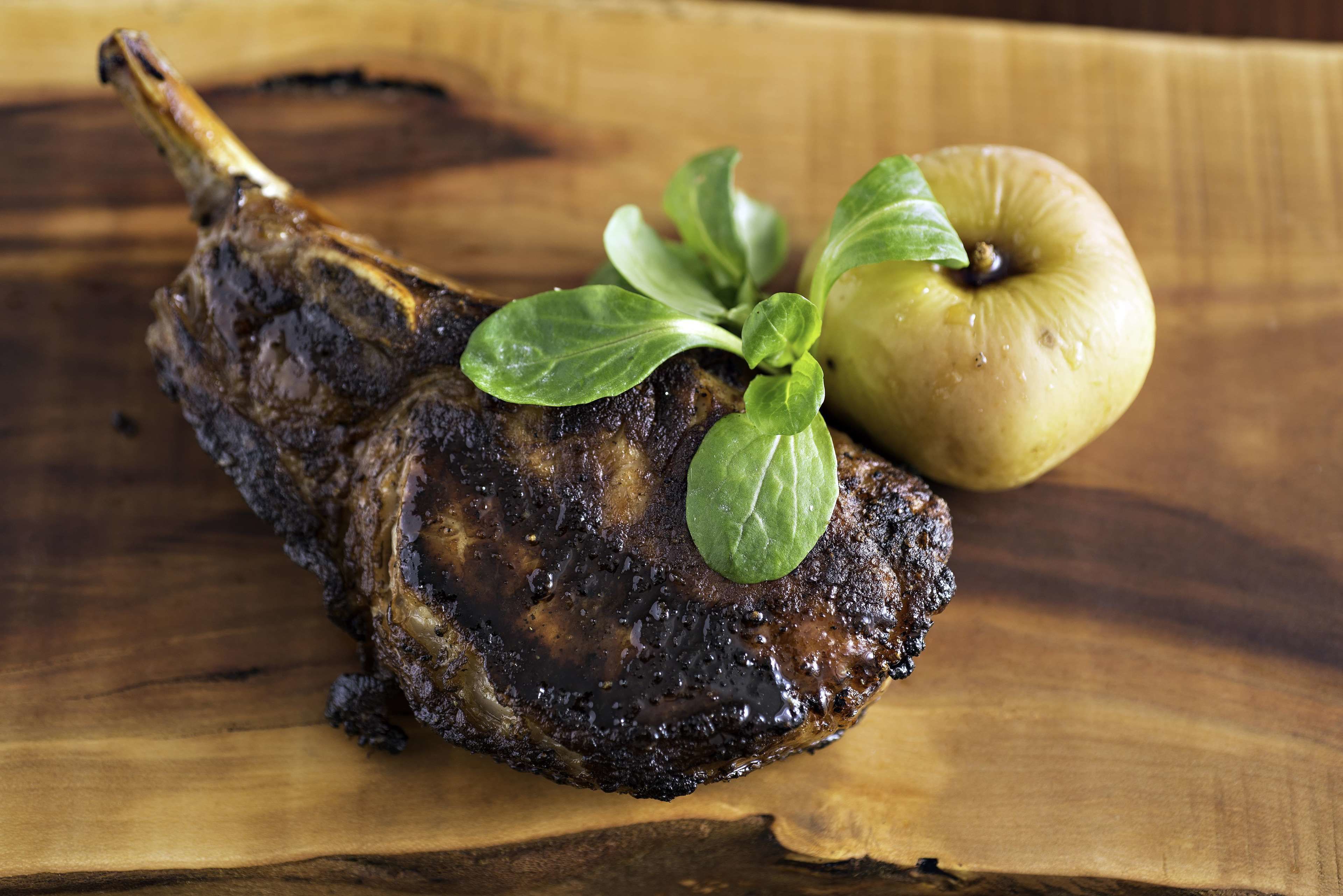 A lamb shank with a green leaf garnish on a wooden surface.
