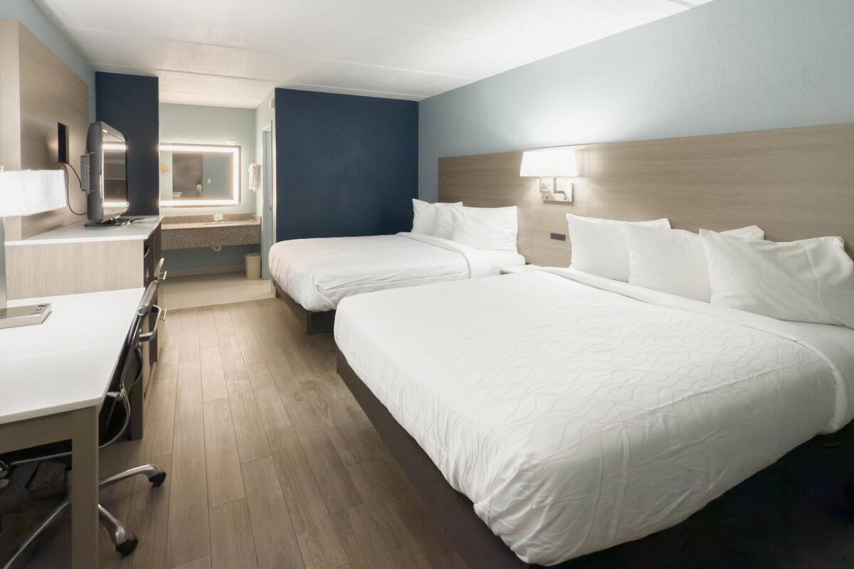 A hotel room with two beds, a desk, a chair, and a mirror.