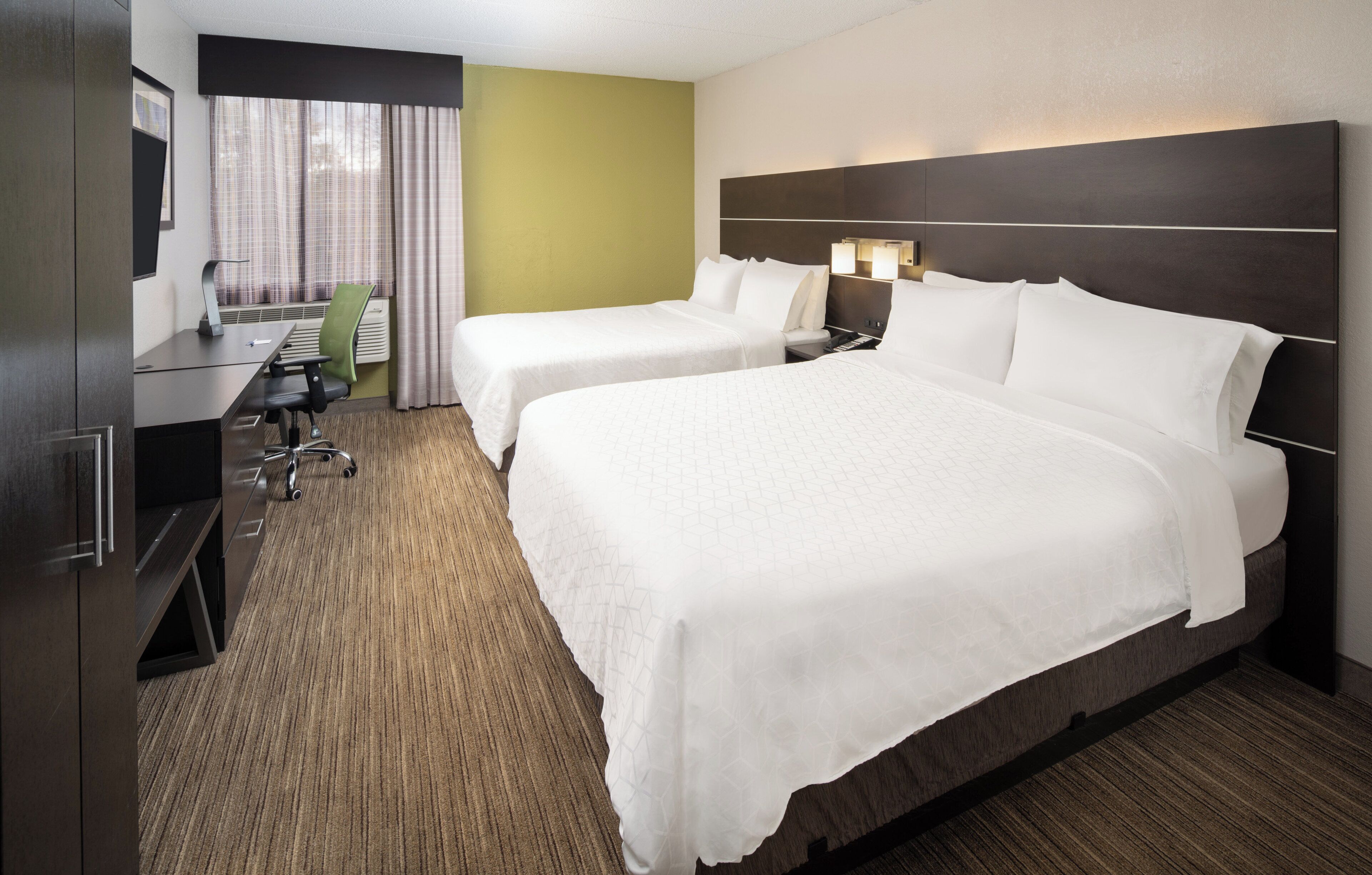 A hotel room with two beds, a desk, a chair, and a TV.