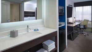 A hotel room with a white sink, mirror, and a desk with a chair. There is a TV on the wall and a window with curtains. - Holiday Inn Express Rochester - Greece by IHG (Rochester)