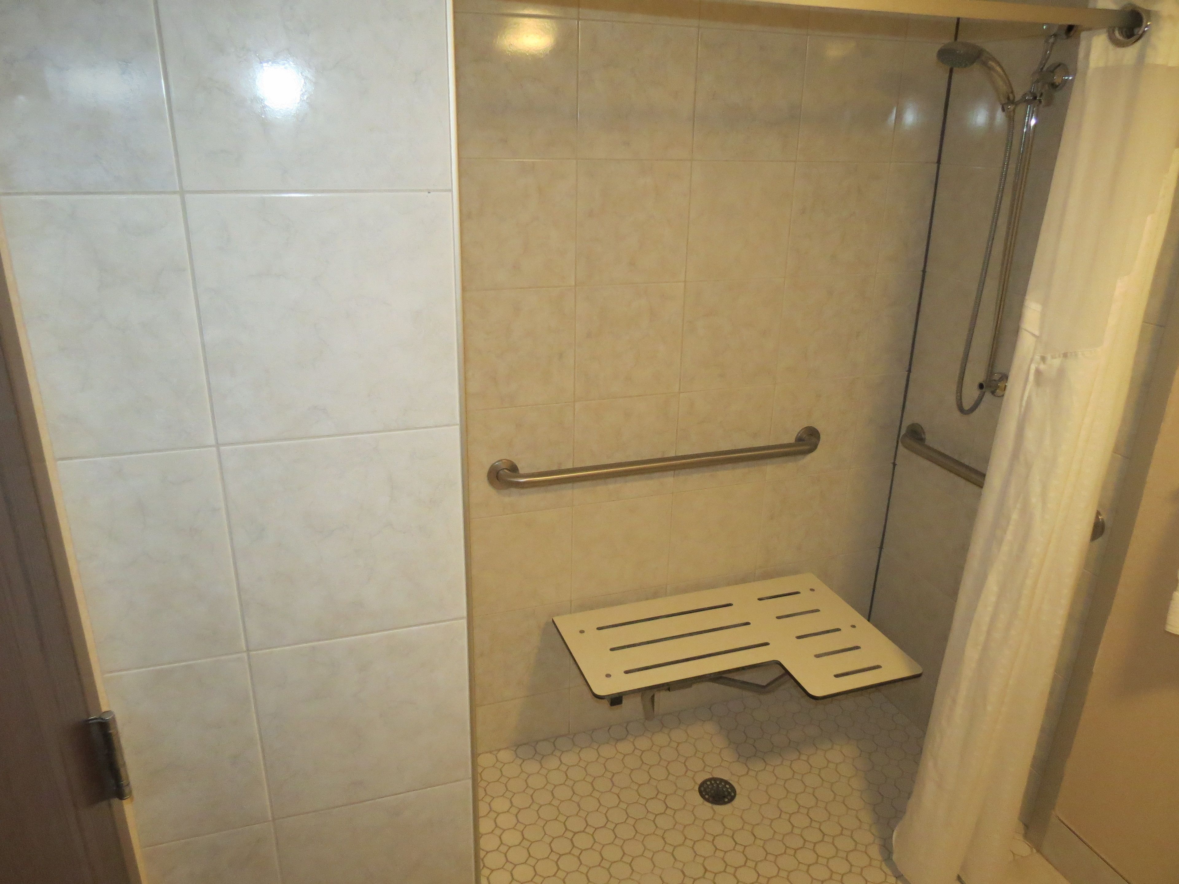A shower with a grab bar, a white tiled floor, and a showerhead.