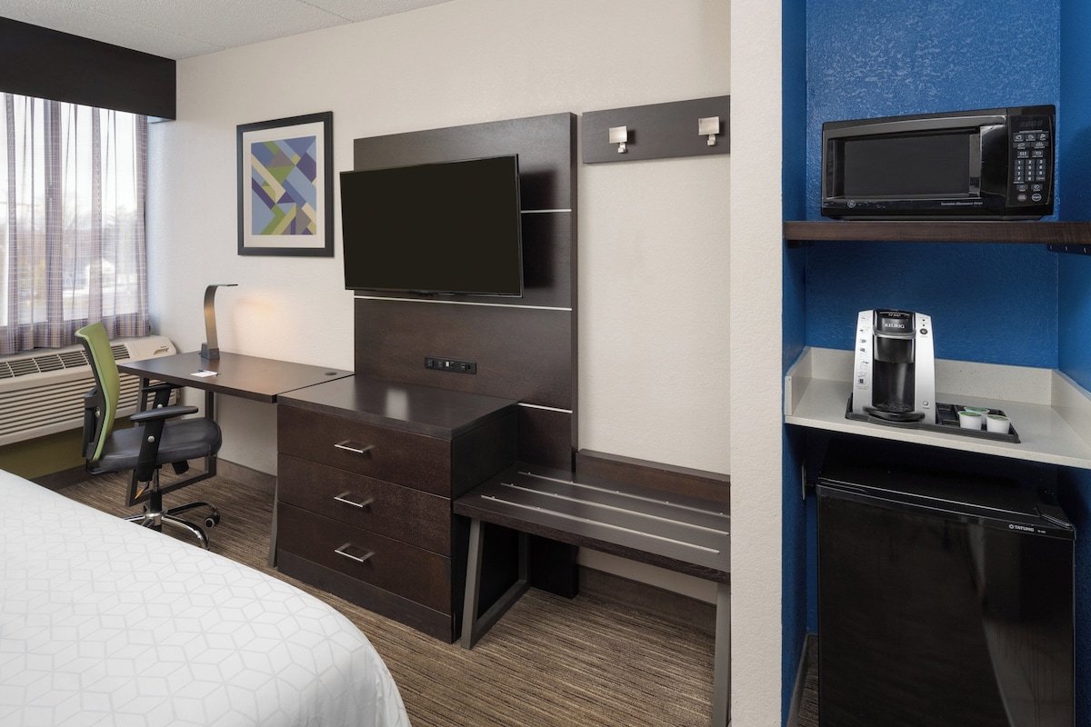 Hotelkamer met een bed, een bureau met stoel, een flatscreen televisie, een minibar en een raam met gordijnen.