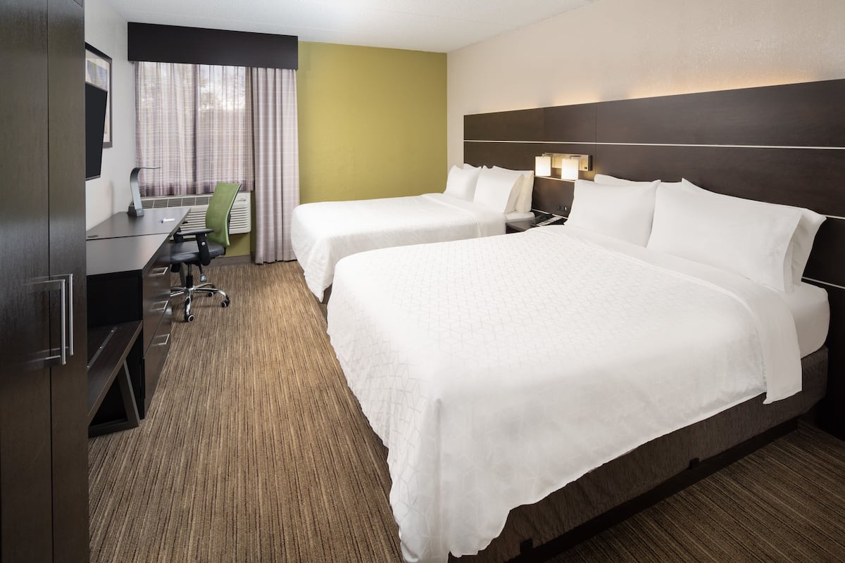 A hotel room with two beds, a desk, a chair, and a TV.