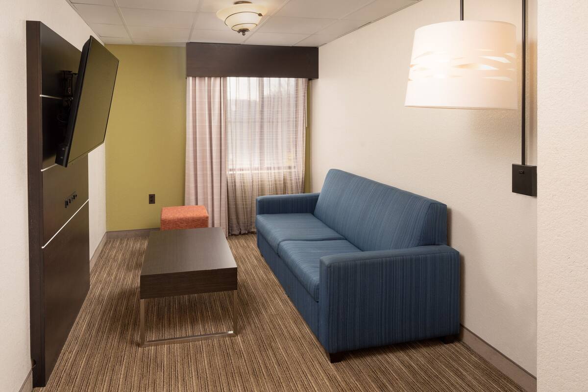 A hotel room with a sofa, a small table, a television, and a lamp.