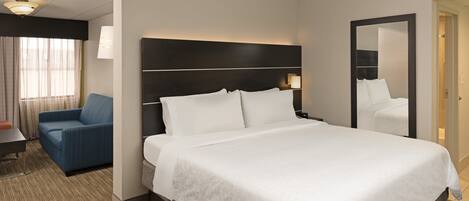 A hotel room with a large bed, a bedside table, a chair, a desk, and a mirror.