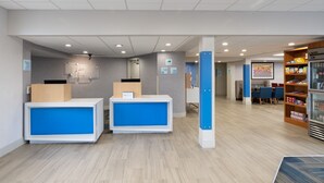 A reception area with two blue counters, a snack bar, and a seating area with tables and chairs. - Holiday Inn Express Rochester - Greece by IHG (Rochester)
