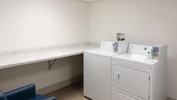 A laundry room with a washing machine, dryer, and a blue chair.