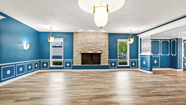 A spacious room with a stone fireplace, wooden flooring, and blue walls with white trim. - HomeTowne Studios by Red Roof Yuba City Bonanza – Marysville (Yuba City)