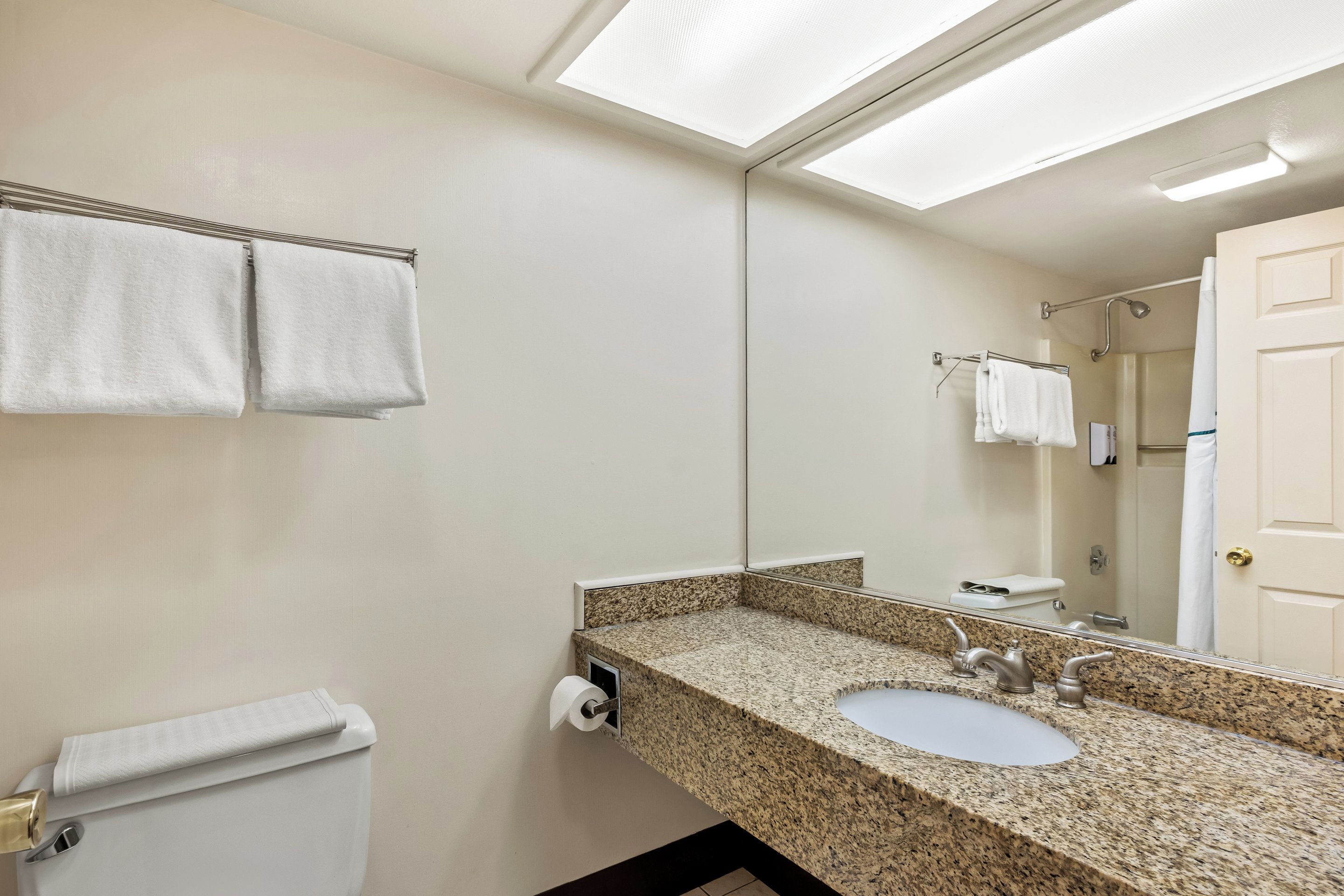 A bathroom with a granite countertop sink, a toilet with a towel, and a mirror reflecting a shower area.