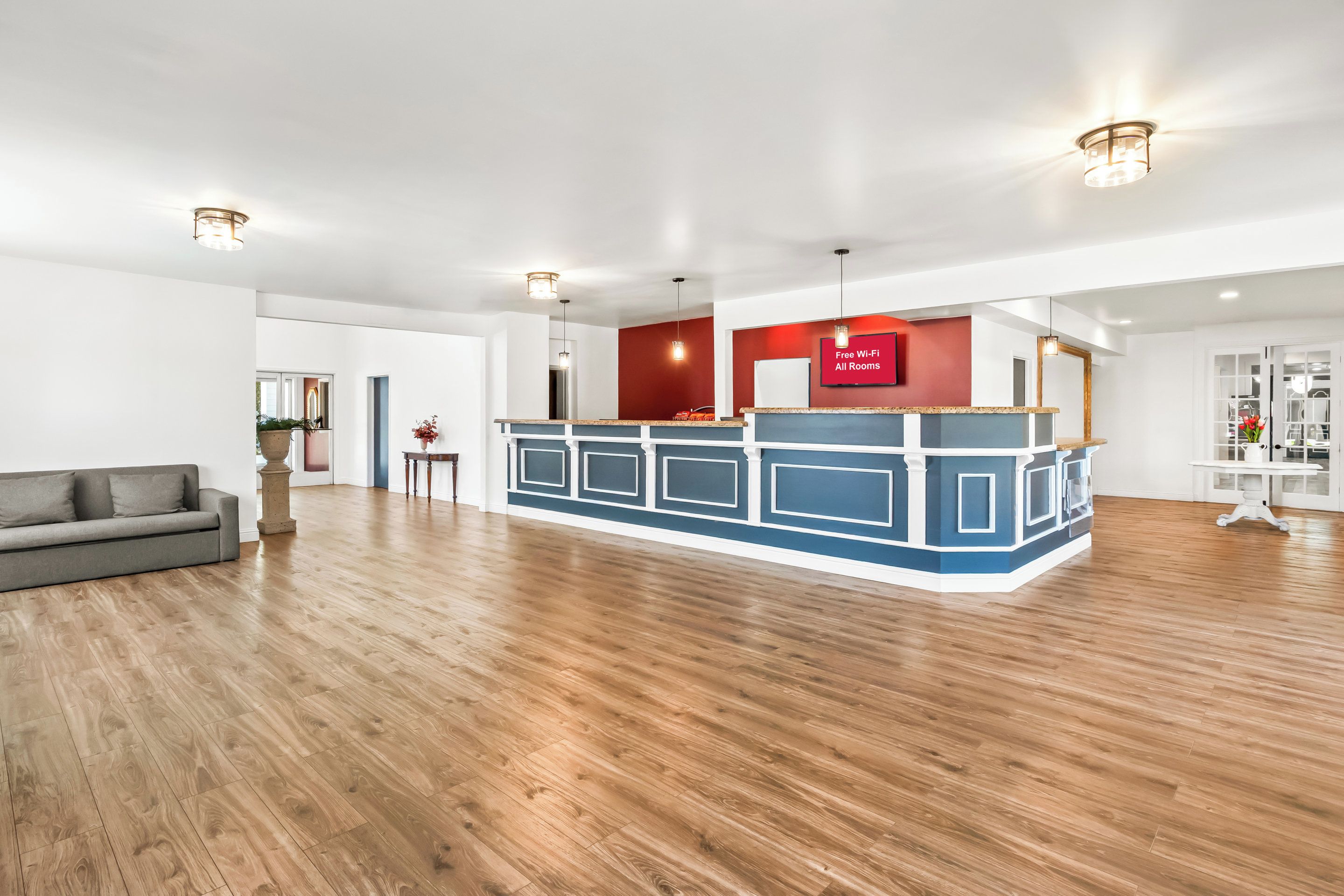 Een ruime hotel lobby met een receptiebalie, een grijze bank en een houten vloer.
