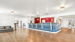 A spacious hotel lobby with a reception desk, a gray sofa, and a wooden floor. - HomeTowne Studios by Red Roof Yuba City Bonanza – Marysville (Yuba City)