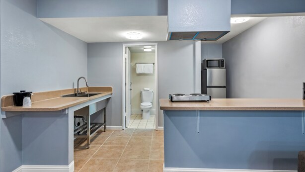A compact kitchen with a sink, microwave, and stove, leading to a bathroom with a toilet and a towel rack. - HomeTowne Studios by Red Roof Yuba City Bonanza – Marysville (Yuba City)