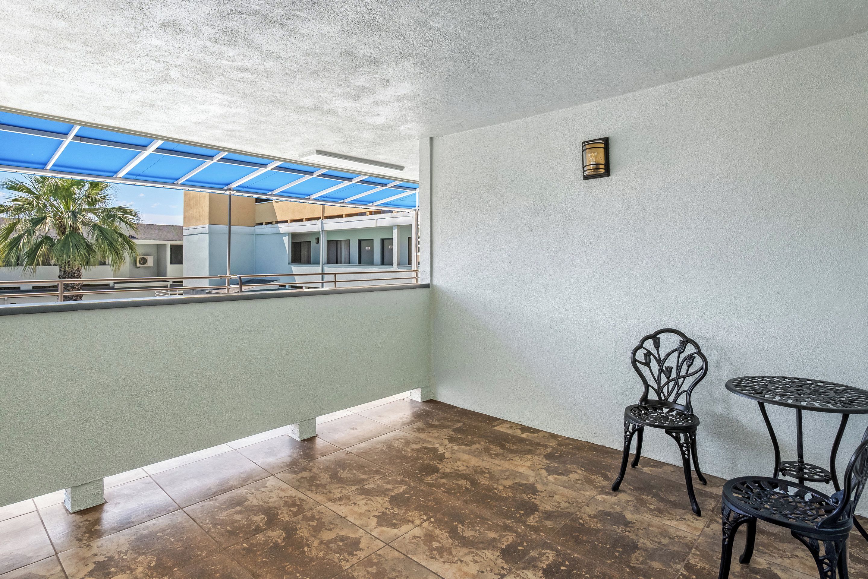 Un balcon donnant sur un immeuble et des palmiers, avec deux chaises en métal et une petite table.