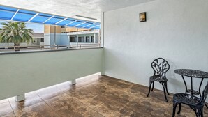 Un balcon donnant sur un immeuble et des palmiers, avec deux chaises en métal et une petite table.