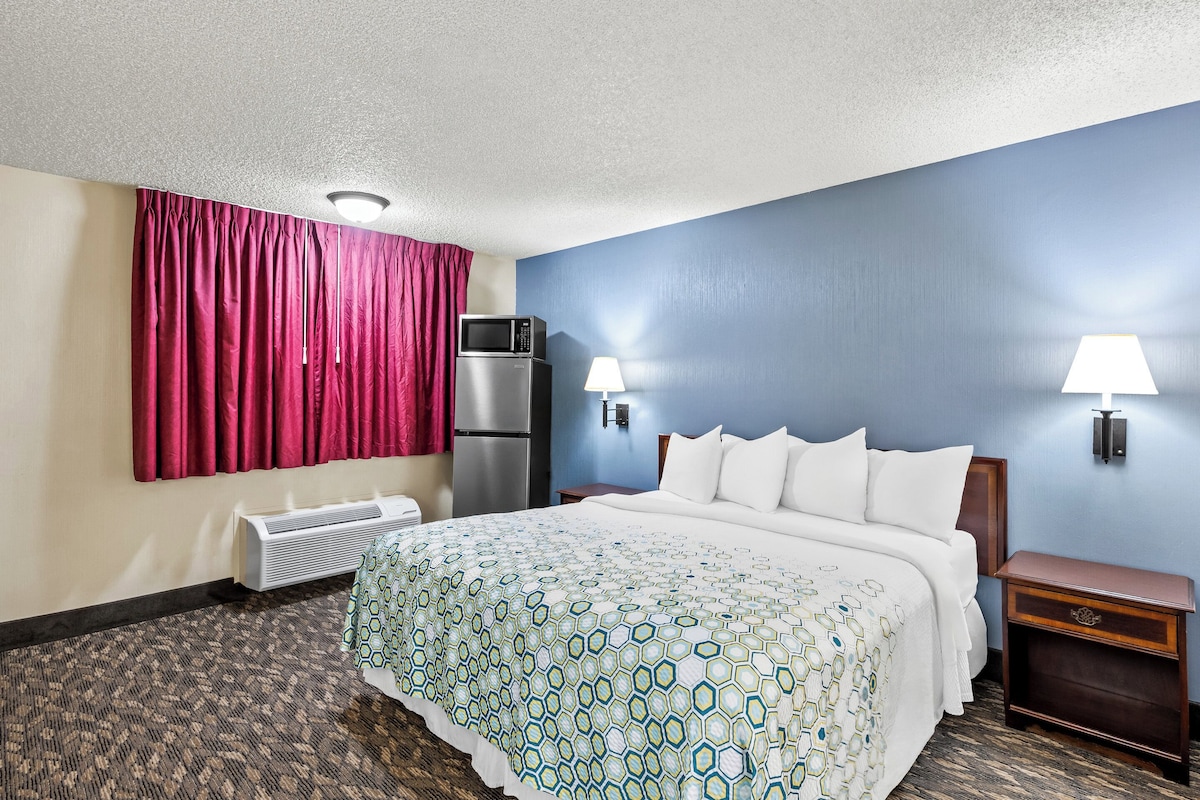 Una habitación de hotel con cama, calefactor, microondas, mesita de noche y dos lámparas de pared.