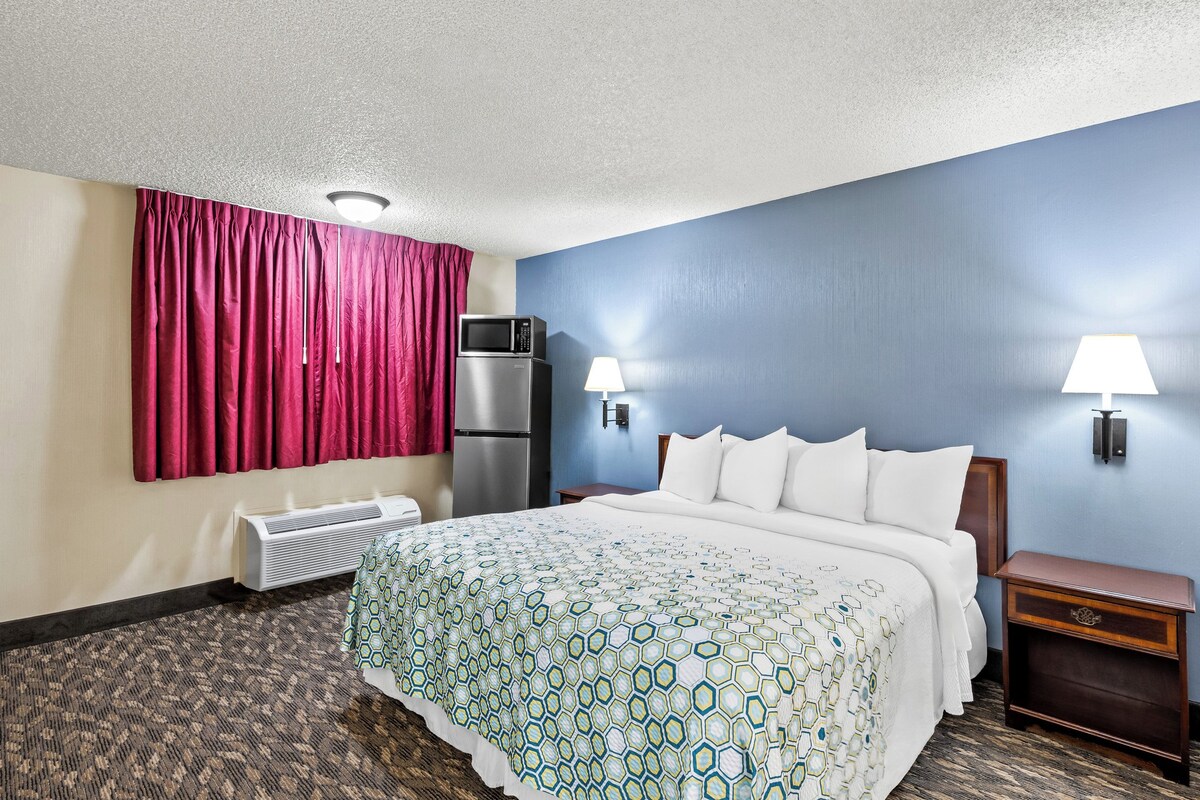 A hotel room with a bed, a heater, a microwave, a nightstand, and two wall-mounted lamps.