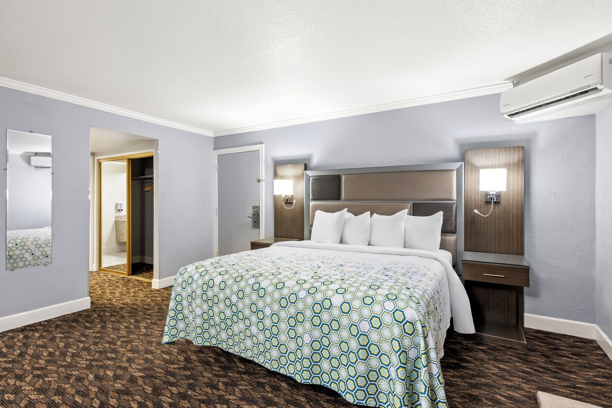 A hotel room with a large bed, a nightstand, a wall-mounted TV, and a door leading to a bathroom.