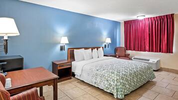 A hotel room with a bed, a desk, a chair, two bedside lamps, a window with red curtains, and an air conditioning unit.