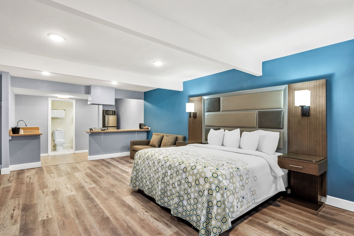 Un dormitorio moderno con una cama grande, una mesita de noche, un aparador y un baño visible a través de una puerta abierta.
