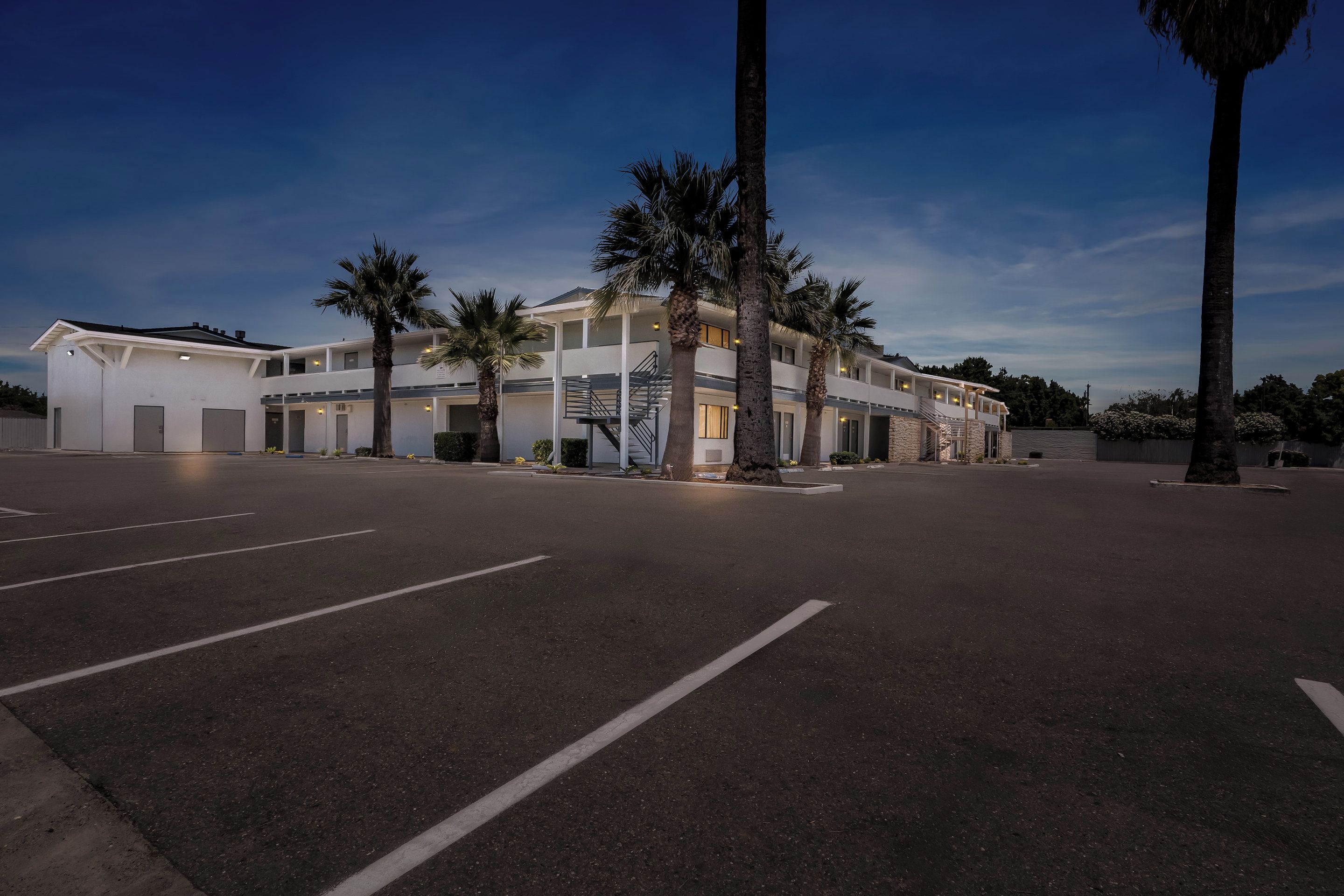 Un hotel de varios pisos con estacionamiento y palmeras.