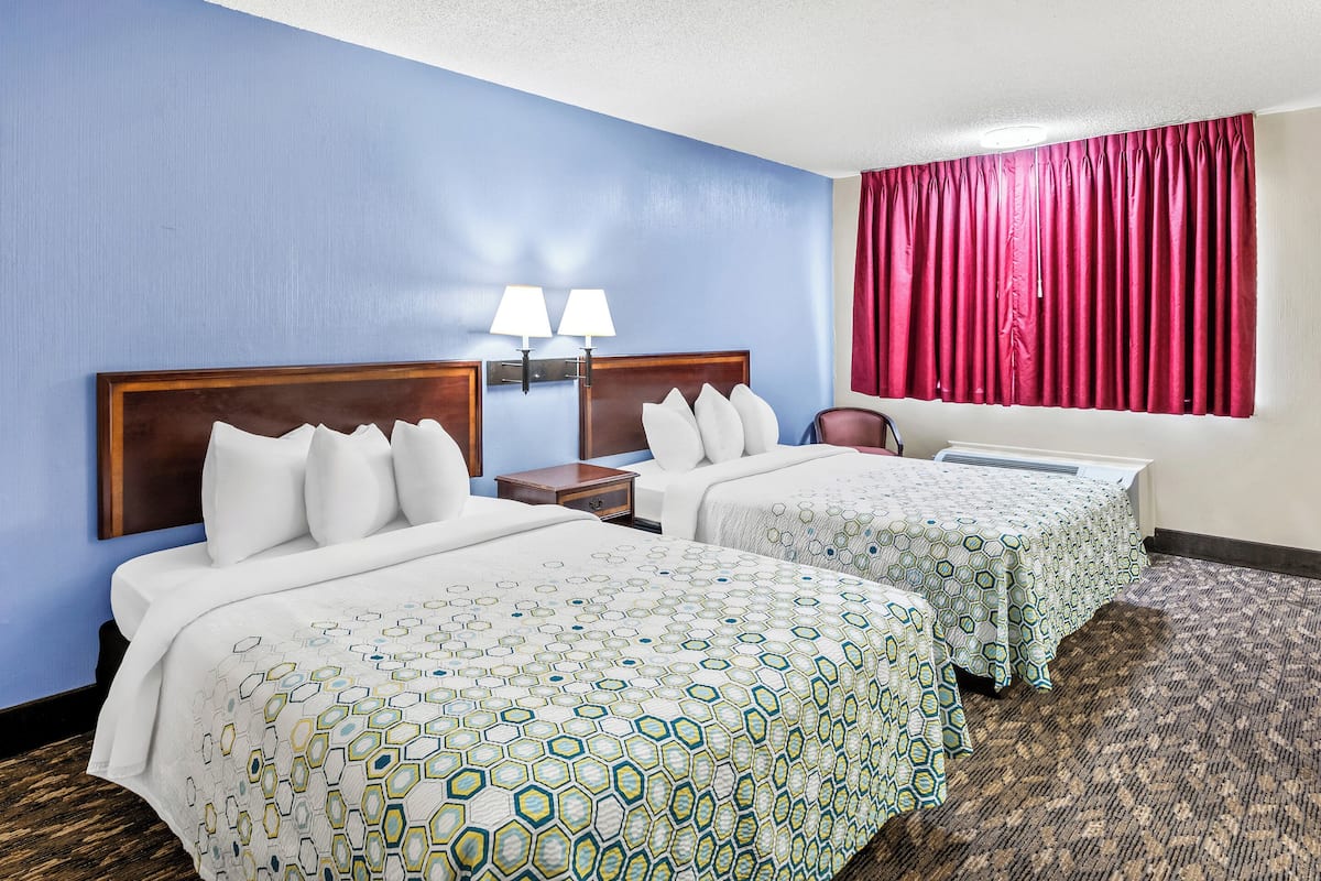 A hotel room with two beds, a nightstand, and a window with red curtains.
