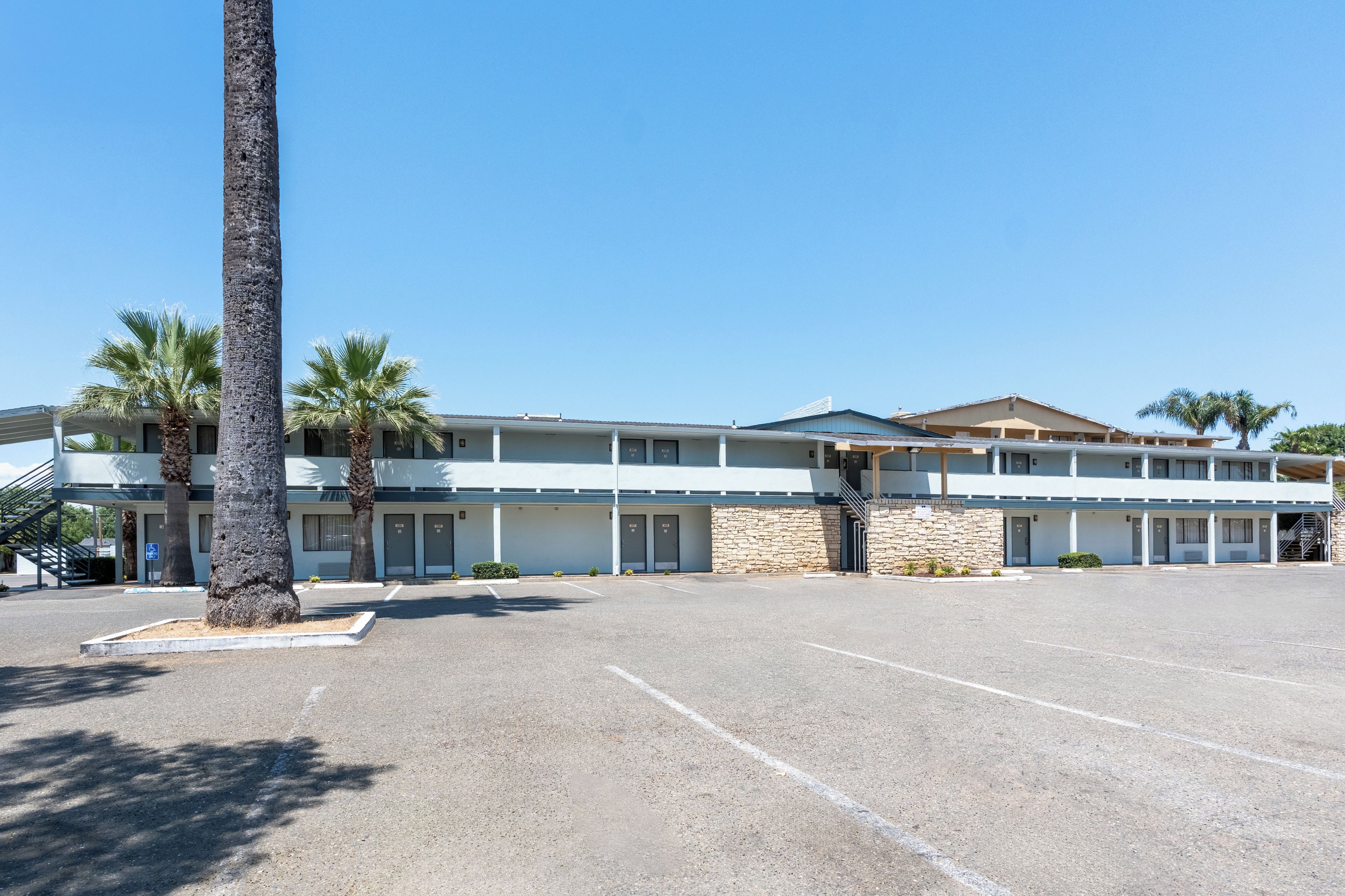 A motel with a parking lot, palm trees, and a two-story building with a flat roof.