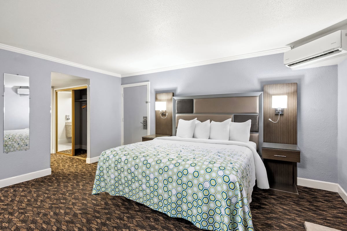 A hotel room with a large bed, a nightstand, a wall-mounted TV, and a door leading to a bathroom.