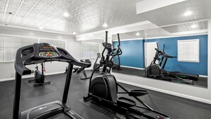 A gym with exercise equipment, a mirrored wall, and a blue accent wall. - HomeTowne Studios by Red Roof Yuba City Bonanza – Marysville (Yuba City)