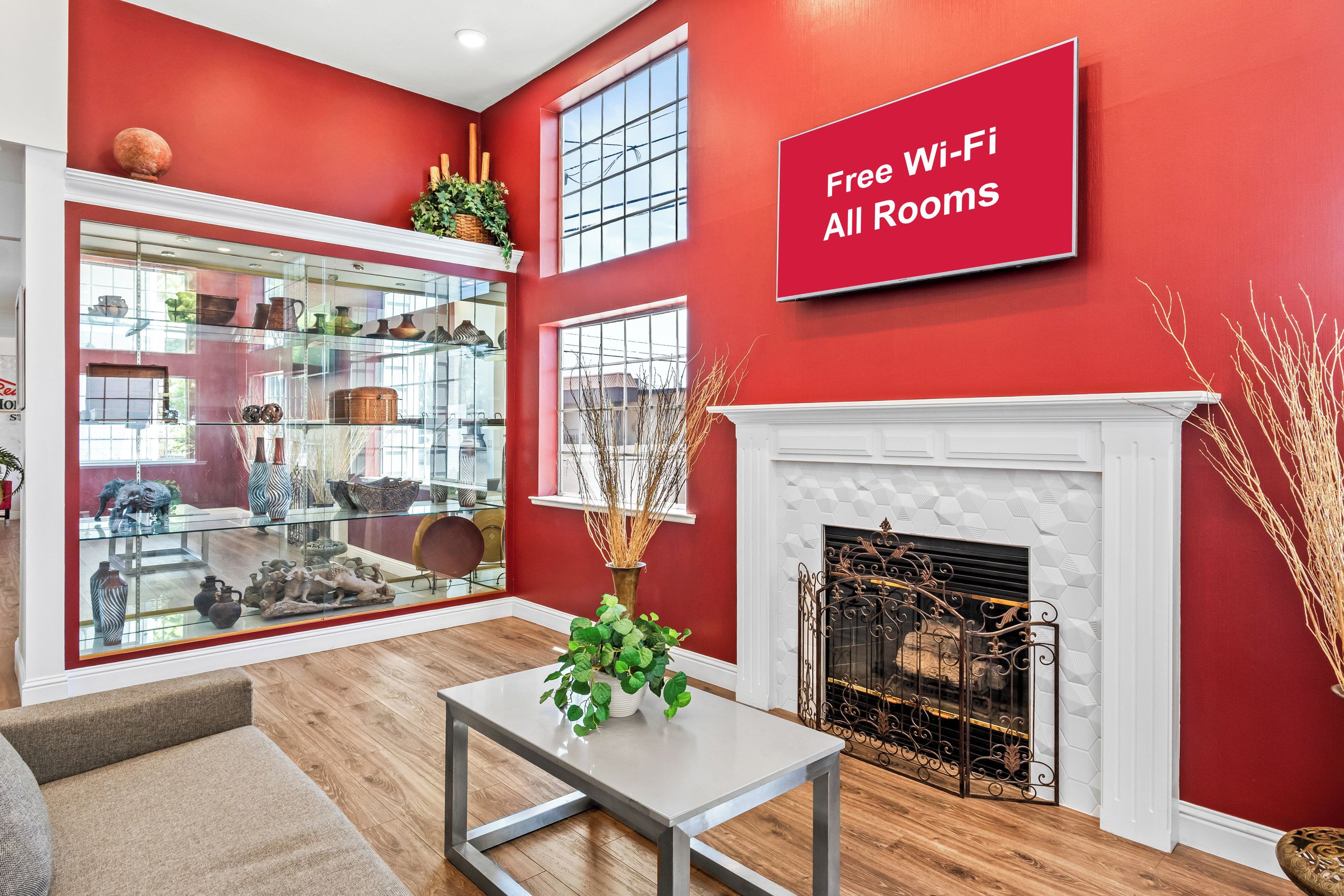 Una sala de estar moderna con una pared roja, una chimenea y una vitrina de vidrio llena de objetos decorativos.