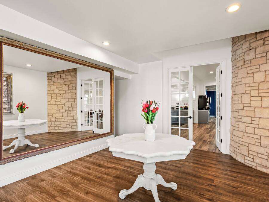 A room with a white pedestal table, a large mirror, and a vase with flowers.