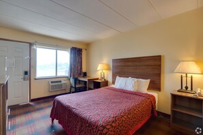 Hotelkamer met een bed, bureau, stoel, twee lampen, een raam met gordijnen en een deur.