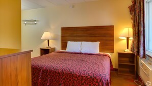 Een hotelkamer met een houten hoofdbord, twee bedlampen, een bed met een bloemenprint sprei, een houten nachtkastje en een raam met gordijnen.