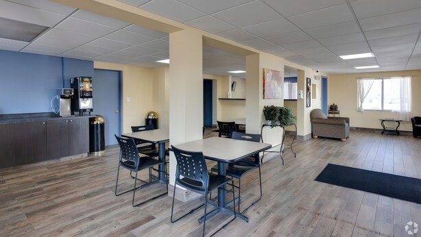 Een ruime kamer met een grote eettafel, stoelen, een bank en een koffieapparaat.