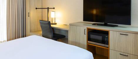 A hotel room with a bed, a desk with a chair, a flat-screen TV, a microwave, and a wardrobe.